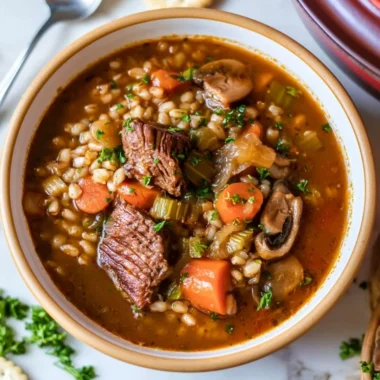 Hearty beef barley soup with fresh vegetables and herbs in a bowl