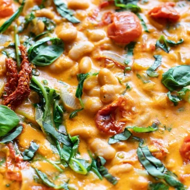 Creamy vegan tomato white bean stew in a bowl with herbs on top.