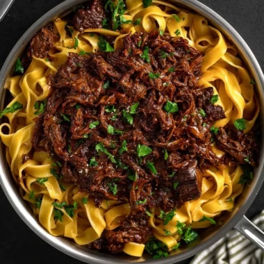Bowl of slow-cooked short rib ragù with pasta and fresh herbs