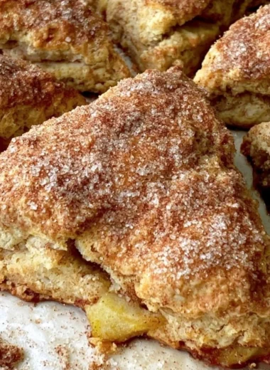 Freshly baked apple scones on a wooden table, sprinkled with cinnamon.