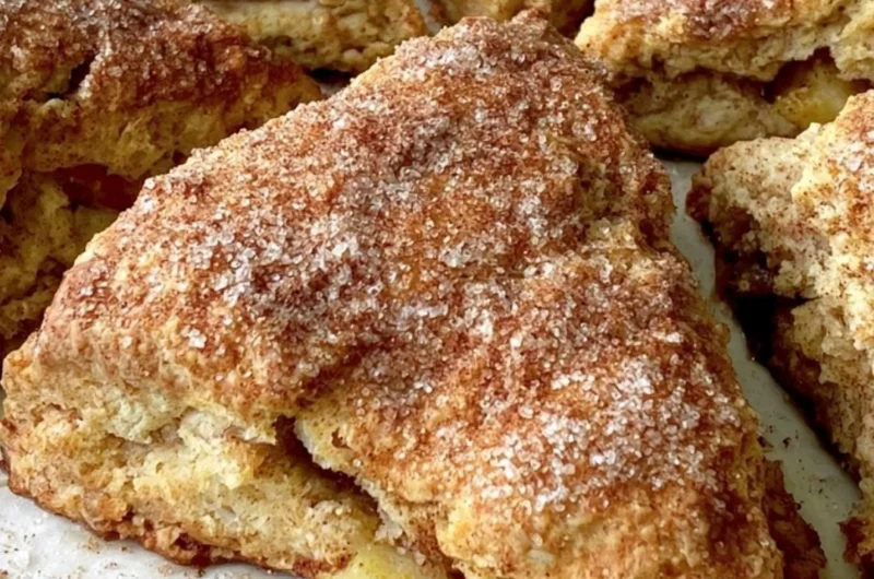 Freshly baked apple scones on a wooden table, sprinkled with cinnamon.