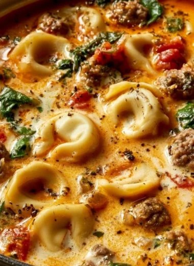 Bowl of Italian Sausage Tortellini Soup with fresh herbs and cheese on top.