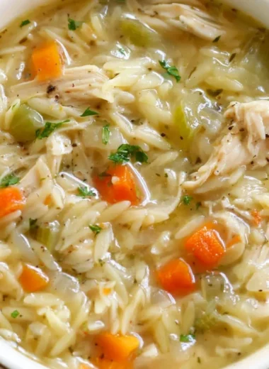 Bowl of Lemon Chicken Orzo Soup with fresh herbs and lemon slices