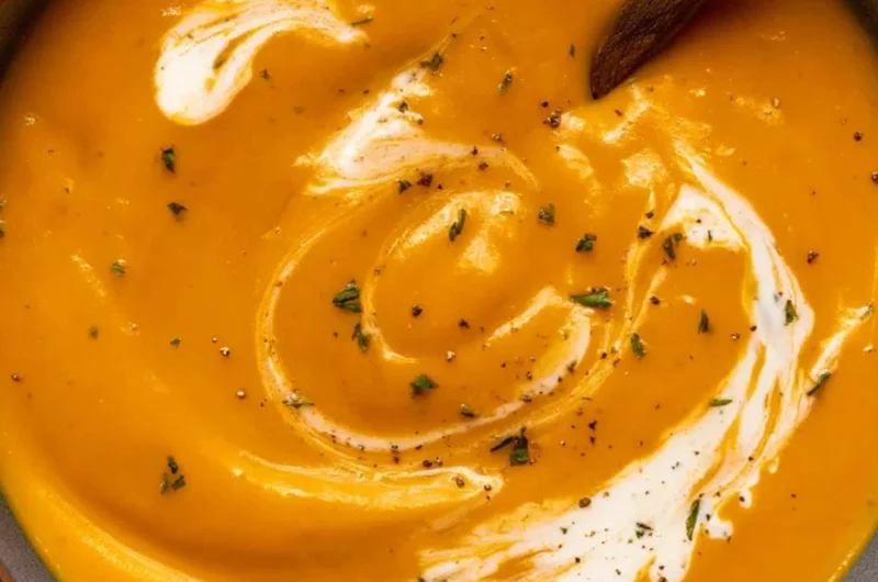 Bowl of creamy maple roasted sweet potato carrot soup garnished with herbs.